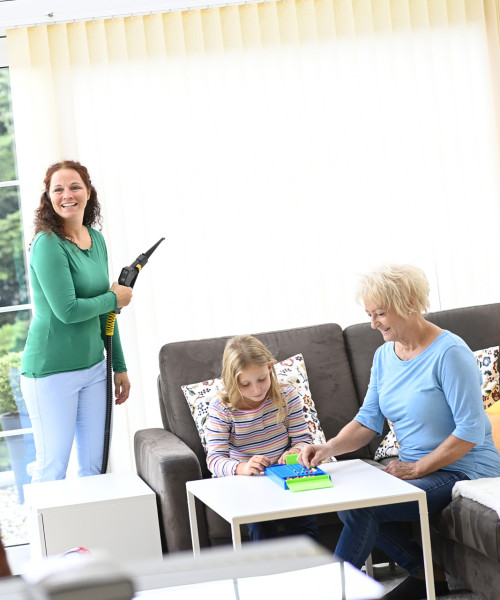 Glückliche Familie im Wintergarten, während Mama die Lamellenvorhänge mit Thermostar Trockendampf reinigt.