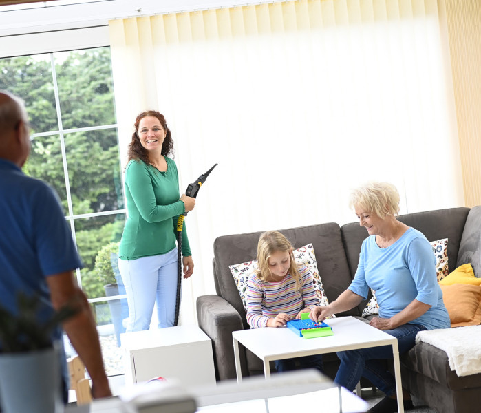 Glückliche Familie im Wintergarten, während Mama die Lamellenvorhänge mit Thermostar Trockendampf reinigt.
